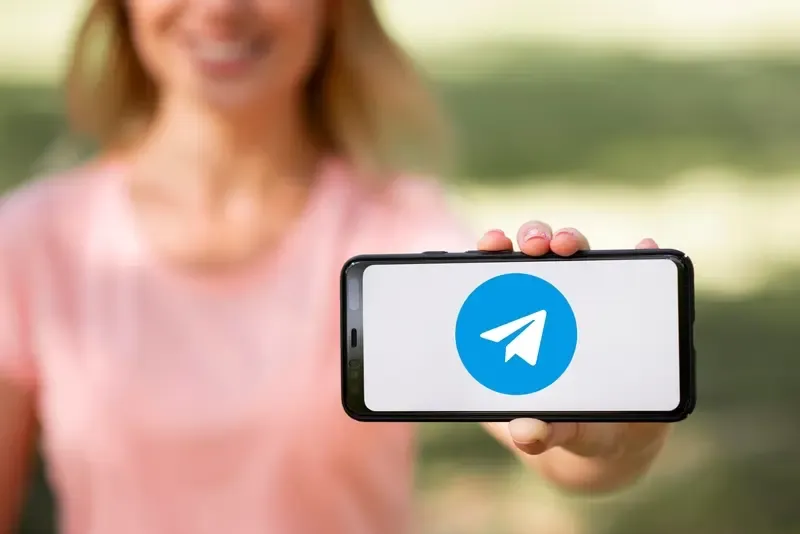 A lady is holding a smartphone showing the Telegram app.