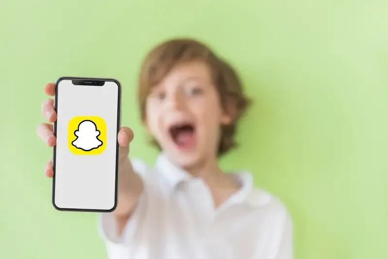 A boy holding a phone with the Snapchat logo on the screen.